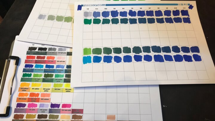 Overlapping printed mixing tables with blue and green ink swatches beside a color reference.